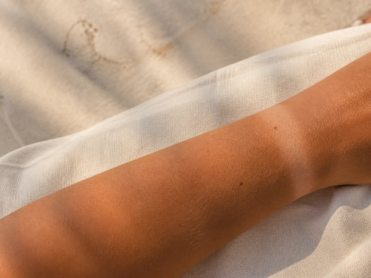 Avant-bras naturellement bronzé posé sur un tissu clair